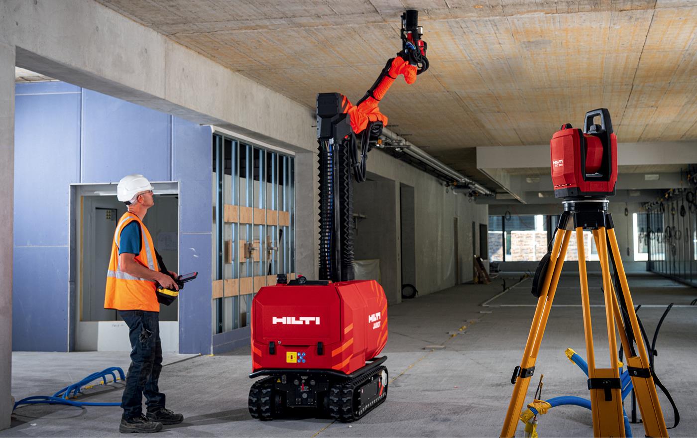 Medarbetare manövrerar en robot som borrar hål i taket i tom lokal.