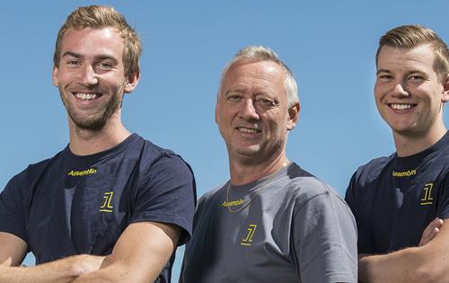 Blå bakgrund och tre leende män med armarna i kors