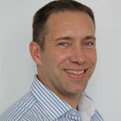 Leende man i blå skjorta är vänd mot kameran för ett porträtt