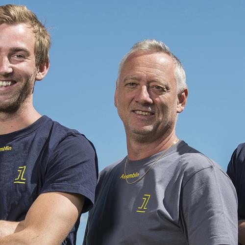 Blå bakgrund och tre leende män med armarna i kors