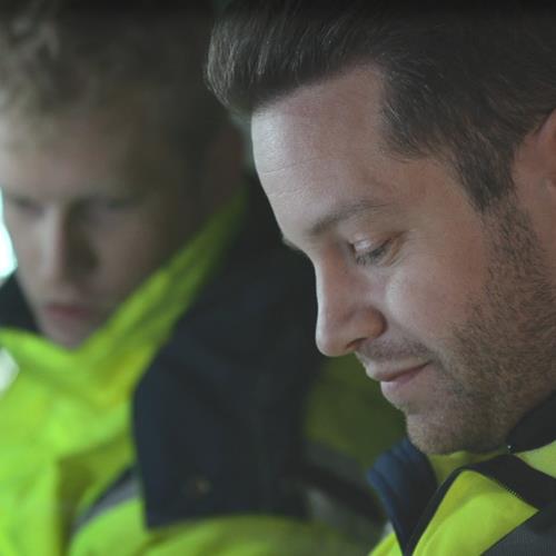 Man i gul jacka och mörka drag tittar neråt i en bil